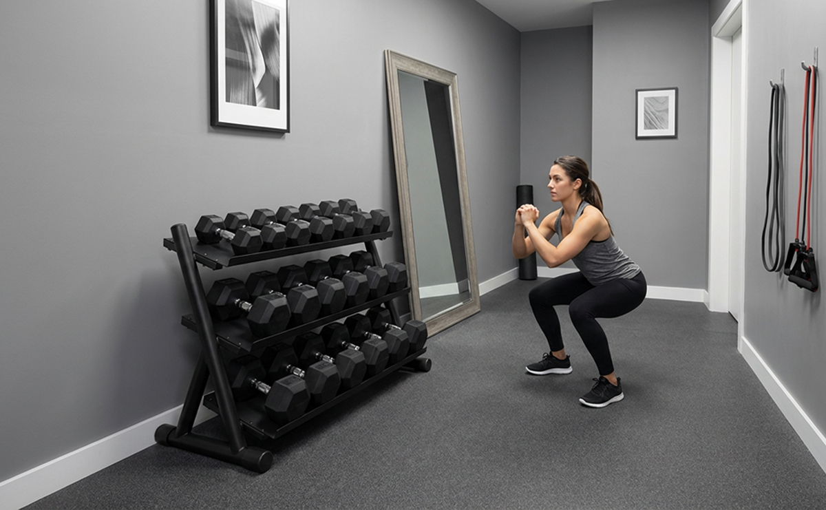 Woman exercising in a home gym with a Vision Fitness 300-DBR Dumbbell Rack.