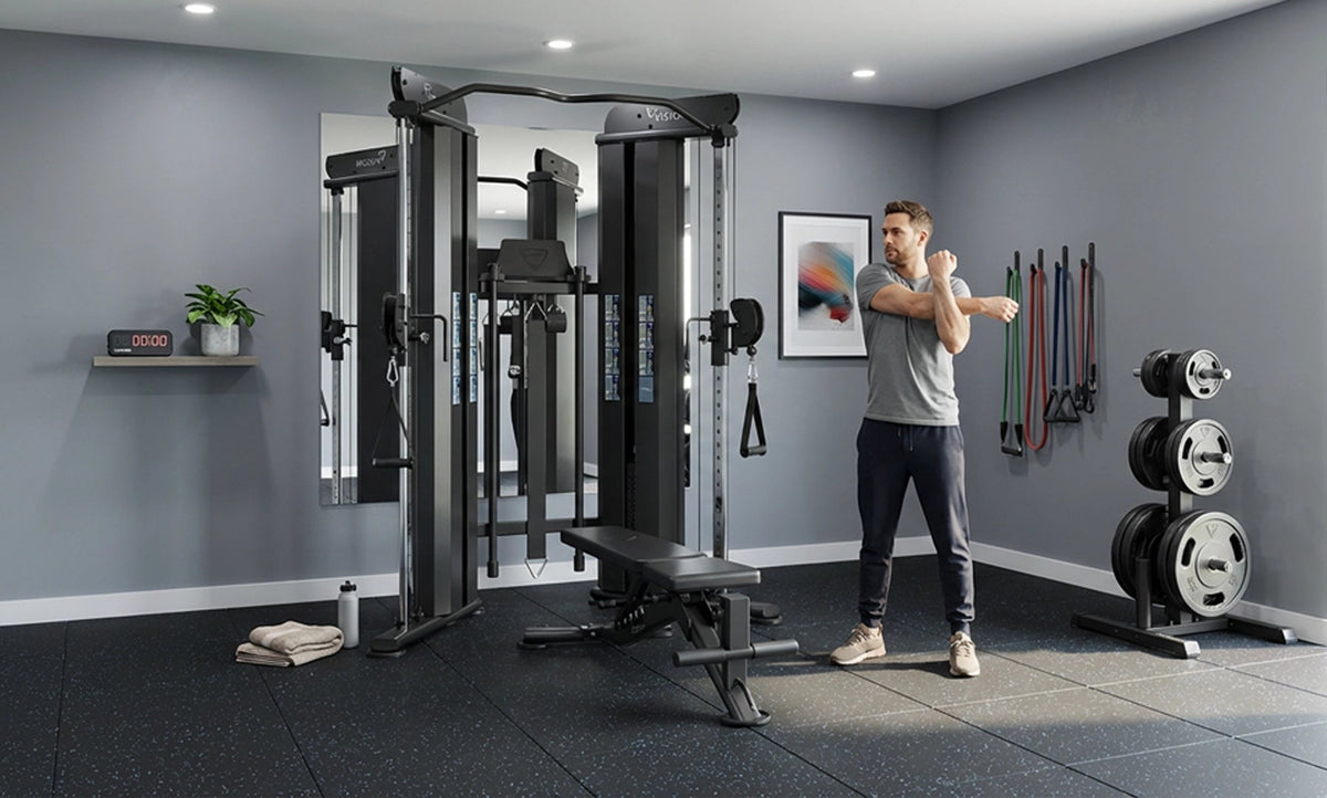 Man stretching next to a Vision Fitness 300-FT Functional Trainer in a home gym with gray walls and other equipment.